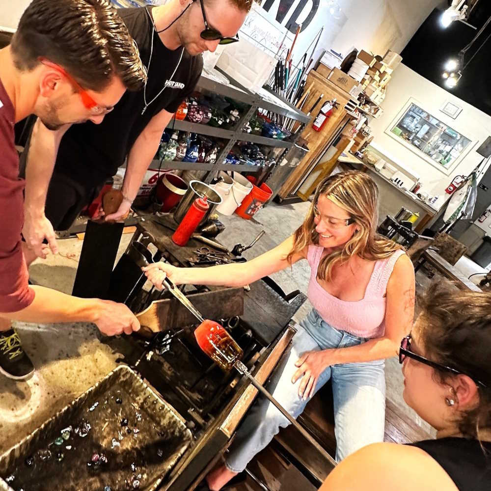 Image of four visitors blowing glass of Hot Sand glassblowing studio in Asbury Park.