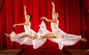 two dancers jumping on stage with a red curtain backdrop performing with the Do Portugal Circus