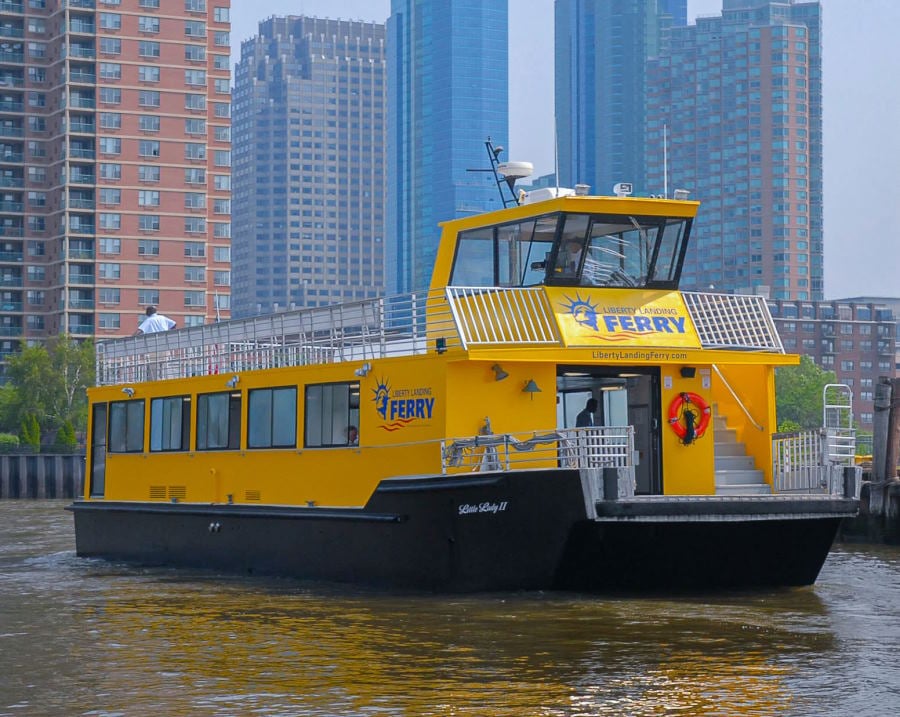 Beautiful yellow liberty landing ferry with Jersey City buildings behind it.